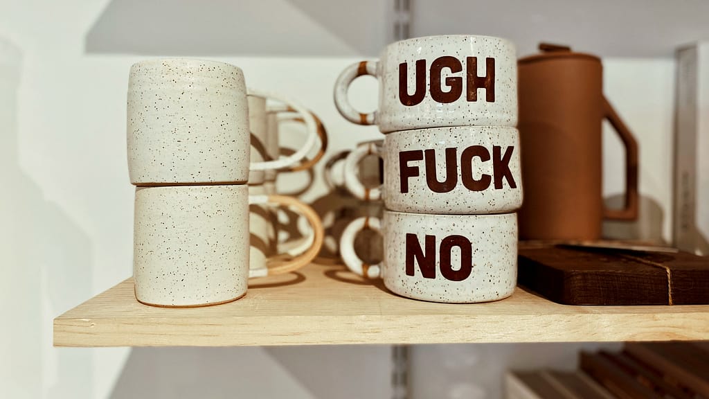 Cups stacked on a shelf. They say "UGH F*CK NO".