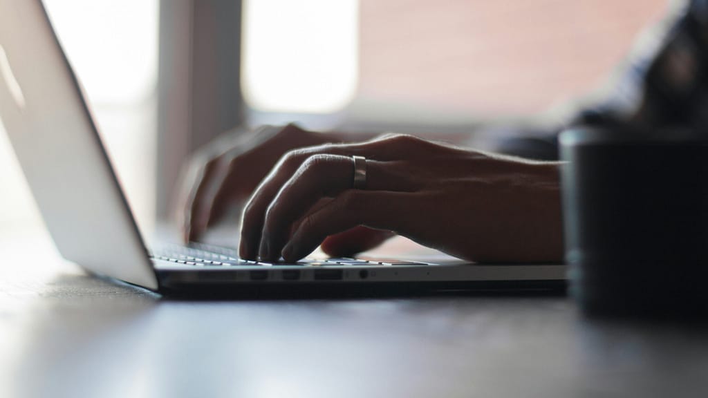 Hands typing on a laptop keyboard with a silver ring on the left ring finger