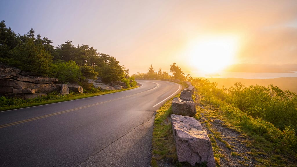 A coastal road goes around a bend. There is a sunset in the background.