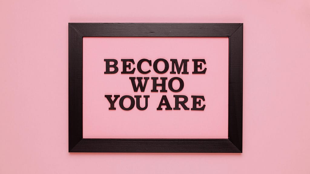 A black frame in front of a pink background. Inside the frame are the words "Become who you are."