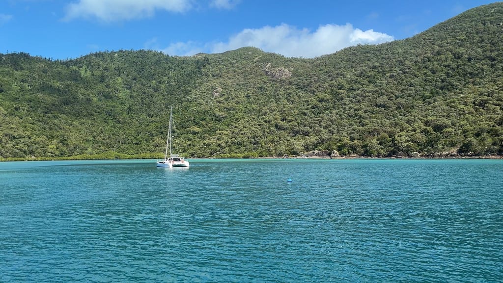 Sailboat on calm turquoise bay with lush green hills and a bright blue sky behind it.