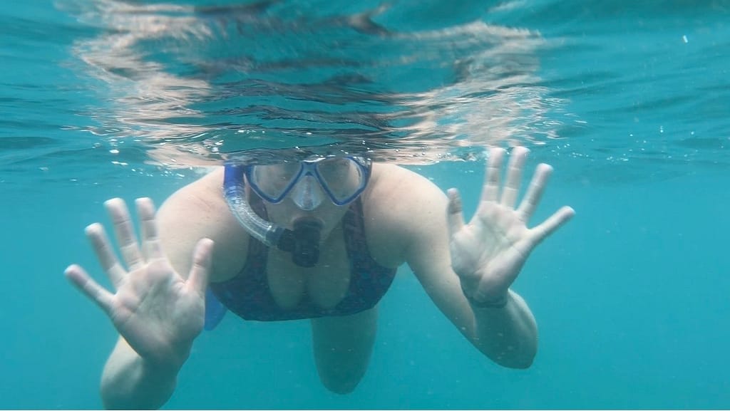 An underwater image of Em snorkelling. She is waving to the camera.