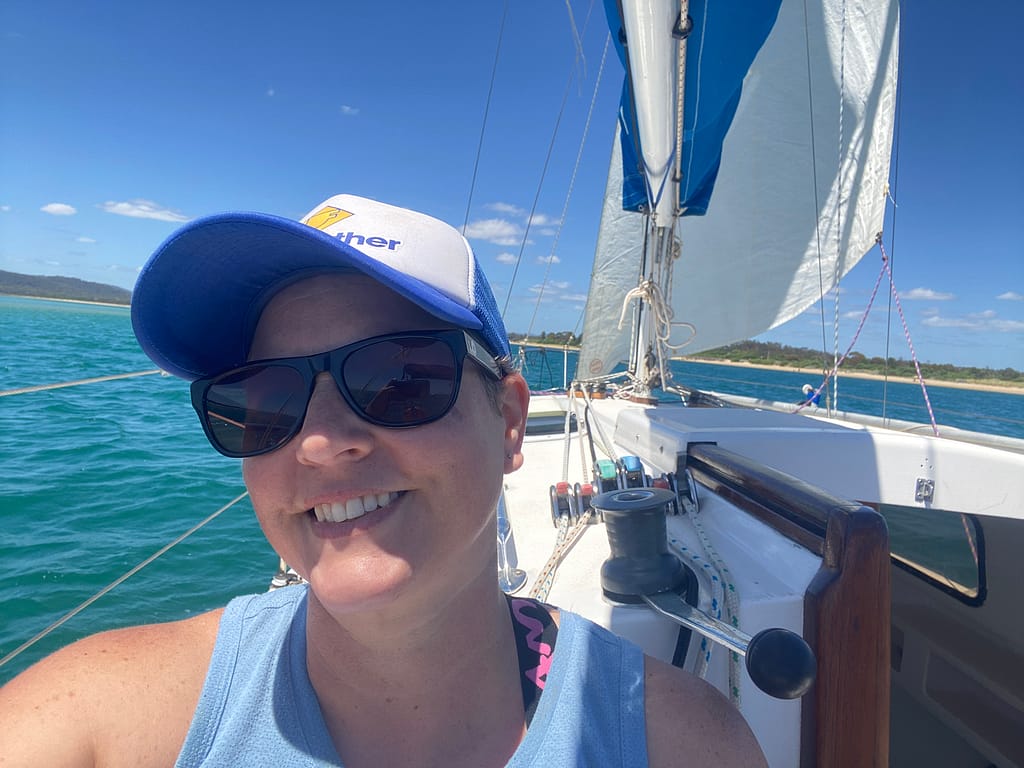 Close up of Em sitting on a sailboat. She is smiling and wearing a cap and sunglasses.