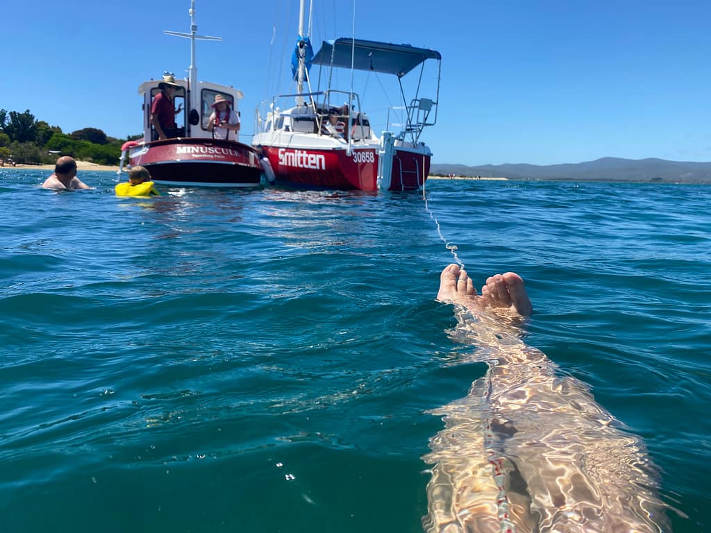 Ems's floating in the water - you can only see her legs - behind two red boats rafted together.
