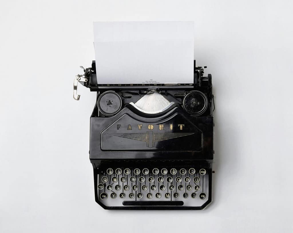 Black and white image of a typewriter and blank paper.