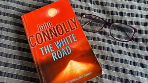 The White Road by John Connolly and a pair of glasses on a bed.