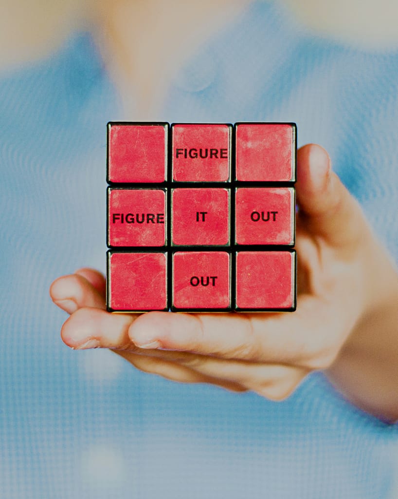 A hand holding a Rubiks cube with the words Figure It Out written on the side.