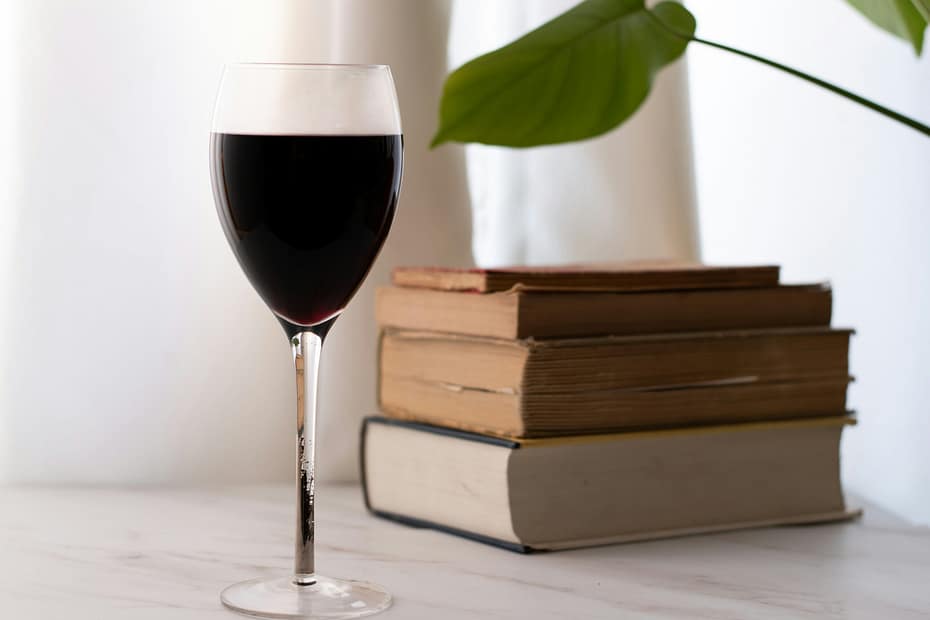 A glass of red wine and a stack of books on a table.