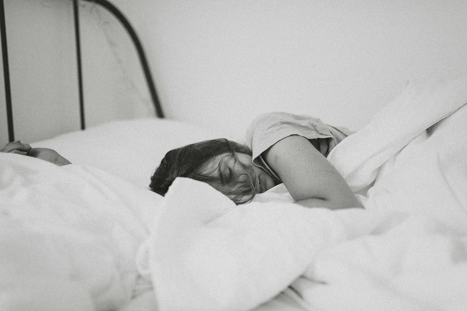 A black and white image of a woman sleeping in bed.