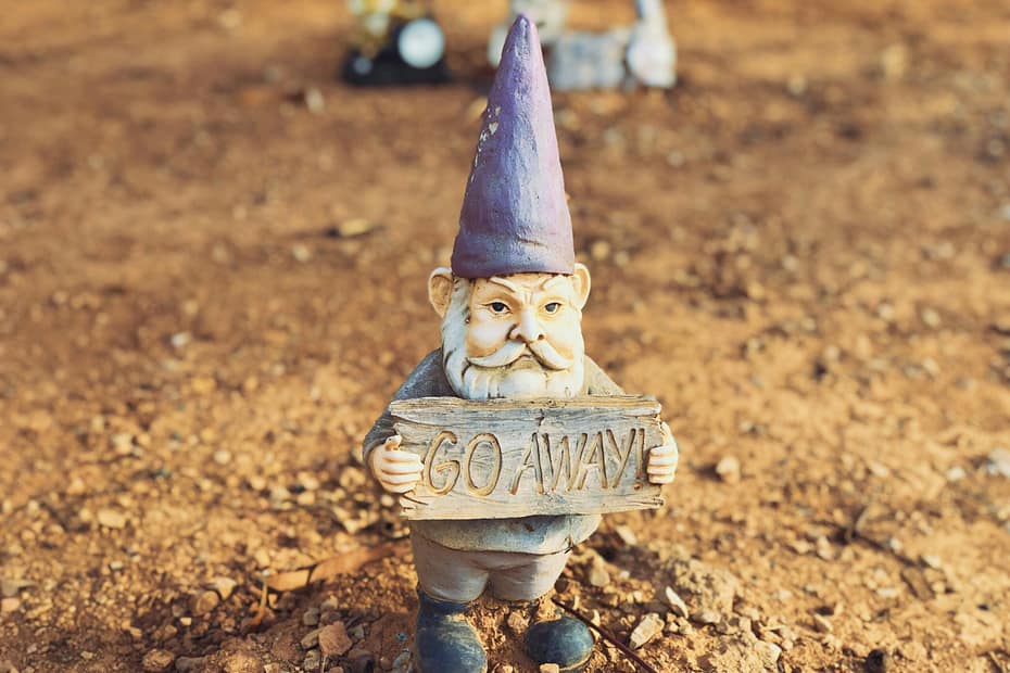 A garden gnome holds a sign that says "go away".