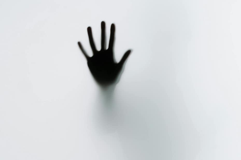 Black and white image. A person places their hand on a frosted screen. Looks eerie.