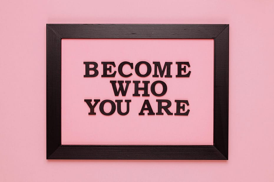 A black frame in front of a pink background. Inside the frame are the words "Become who you are."