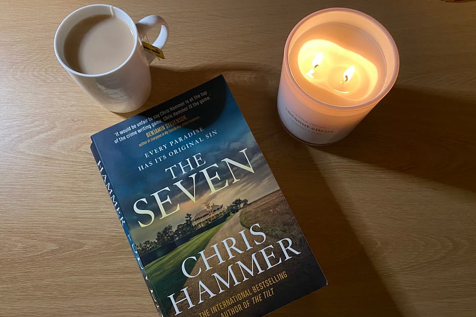 Novel The Seven, but Chris Hammer sits on a desk with a candle and cup of tea.