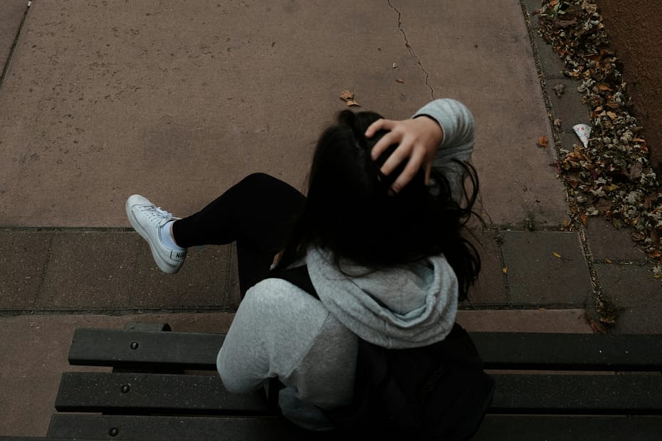 An overhead photo of a woman on a park bench. She has her hand on her head like her mental load is giving her a headache.