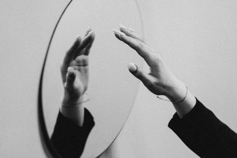 A woman's hand is reflected in an oval mirror on a wall.