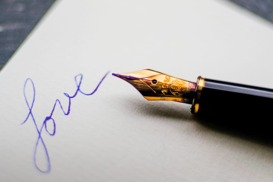 A fountain pen rests on the paper next to the word "Love".