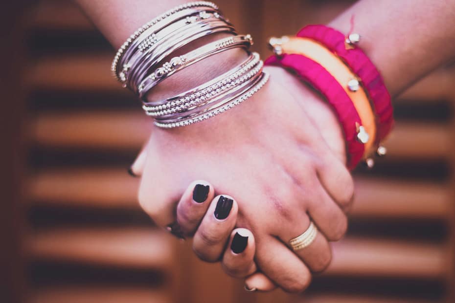 A close-up of two hands clasped together. Two friends holding hands. They are wearing bangles and jewellery.