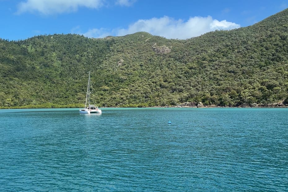 Sailboat on calm turquoise bay with lush green hills and a bright blue sky behind it.