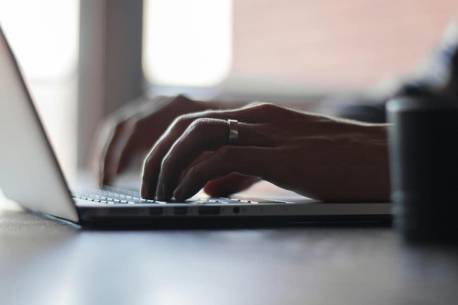 Hands typing on a laptop keyboard with a silver ring on the left ring finger