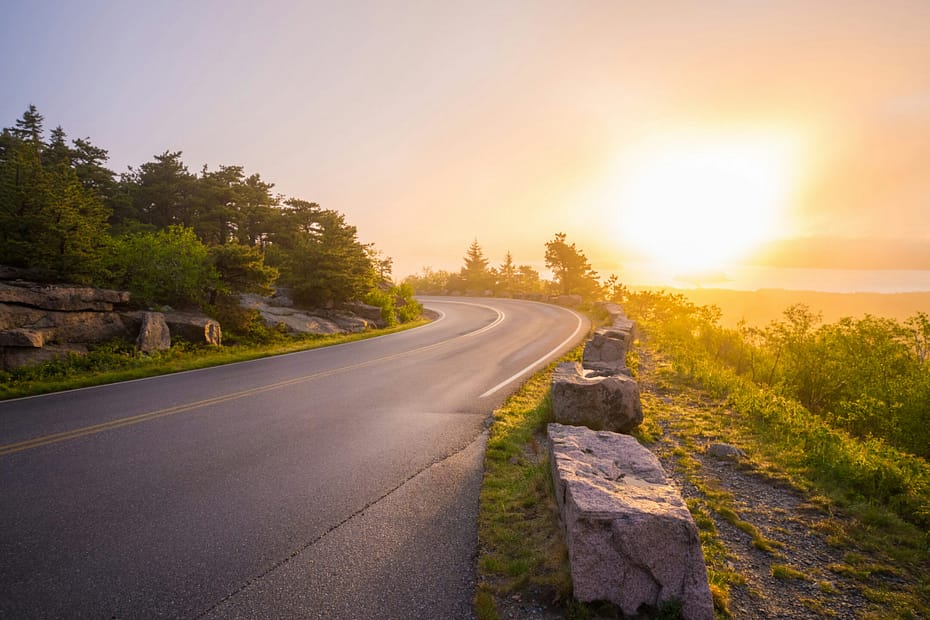 A coastal road goes around a bend. There is a sunset in the background.
